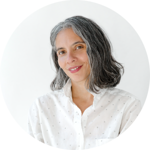 Professional headshot of Tania Velásquez, an educator in massage and manual therapy, known for teaching DermoNeuroModulation. She’s wearing a white collared shirt with small, light grey polka dots, with a gentle smile and a bright, neutral background.